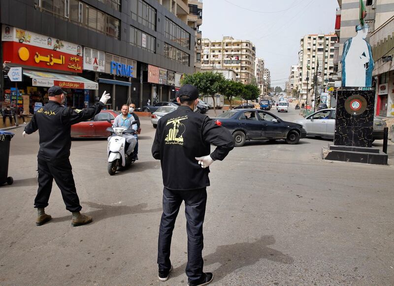 In this Friday, March 27, 2020 photo, Hezbollah members block a road, as others of the Islamic Health Society, an arm of the Iran-backed militant Hezbollah group, spray disinfectant as a precaution against the coronavirus, in a southern suburb of Beirut, Lebanon. Hezbollah has mobilized the organizational might it once deployed to fight Israel or in Syria's civil war to battle the spread of the novel coronavirus. It aims to send a clear message to its Shiite supporters that it is a force to rely on in times of crisis -- particularly after it suffered a series of blows to its prestige. (AP Photo/Bilal Hussein)