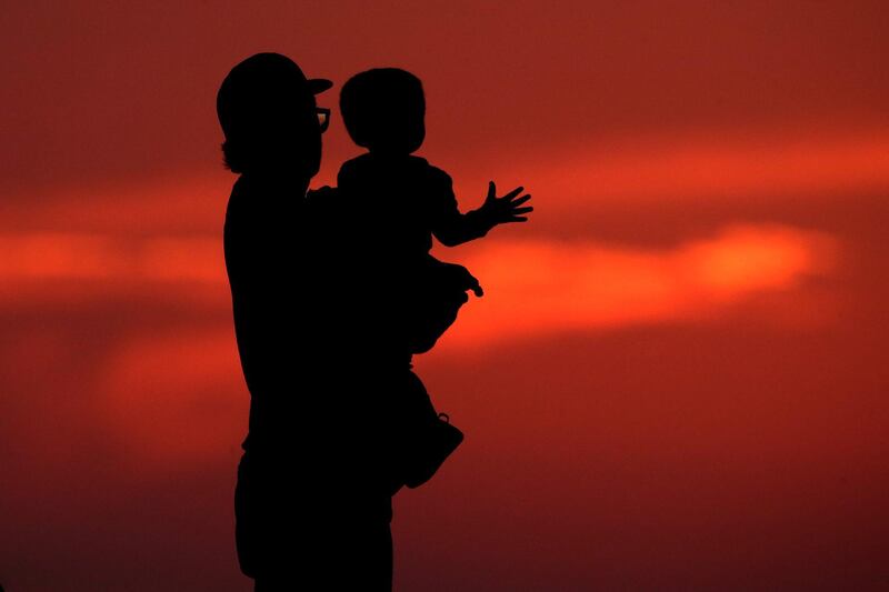 A man and his son are silhouetted against the sky as they watch the sunset from a park in Kansas City, US. AP Photo