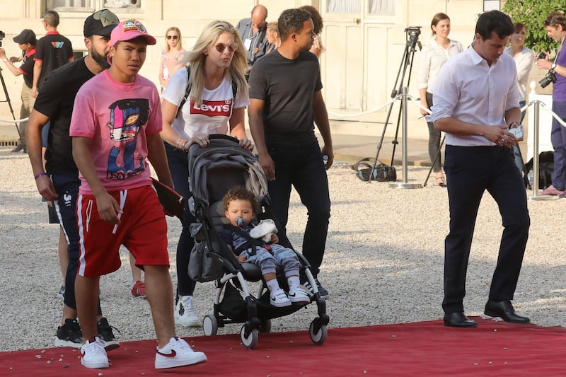 Camille Tytgat (C), wife of France's defender Raphael Varane, pushes their son Ruben sitting in a stroller, as they arrive for a reception at the Elysee Presidential Palace on July 16, 2018 in Paris after French players won the Russia 2018 World Cup final football match. France celebrated their second World Cup win 20 years after their maiden triumph on July 15, 2018, overcoming a passionate Croatia side 4-2 in one of the most gripping finals in recent history. / AFP / ludovic MARIN
