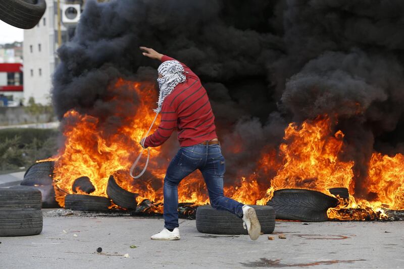 A Palestinian demonstrator holds a sling shot as he runs past burning tyres during clashes with Israeli troops following protests in Ramallah on December 7, 2017. Abbas Momani / AFP