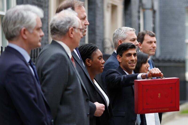 Britain's Chancellor of the Exchequer Rishi Sunak, centre, stands outside No 11 Downing Street and holds up the traditional red box that contains the budget speech for the media, he will then leave to make budget speech to House of Commons, in London, Wednesday, March 11, 2020. Britain's Chancellor of the Exchequer Rishi Sunak will announce the first budget since Britain left the European Union. Sunak is flanked by his team of treasury ministers . (AP Photo/Frank Augstein)