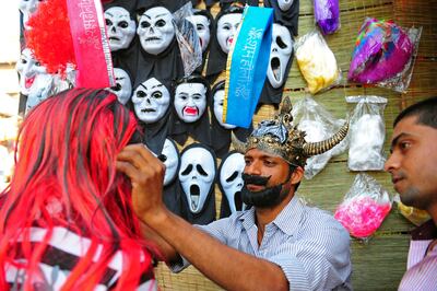 A vendor (C) helps a customer with a wig sold at a roadside shop ahead of the Holi festival in Allahabad on March 15, 2014. Holi, the popular Hindu spring festival of colours, is observed in India at the end of the winter season on the last full moon of the lunar month. AFP PHOTO/ SANJAY KANOJIA (Photo by Sanjay Kanojia / AFP)