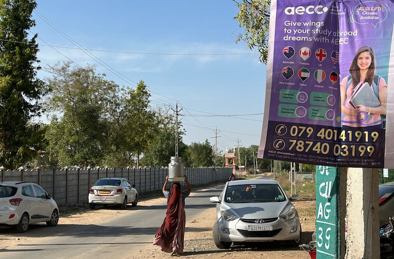 A village woman carrying water walks past a poster advertising visa and immigration services in Nardipur, Gujarat