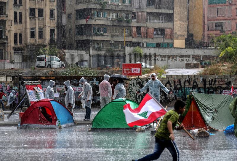 A protester carry Lebanese flag run during rain as protesters close the Achrafieh highway. EPA