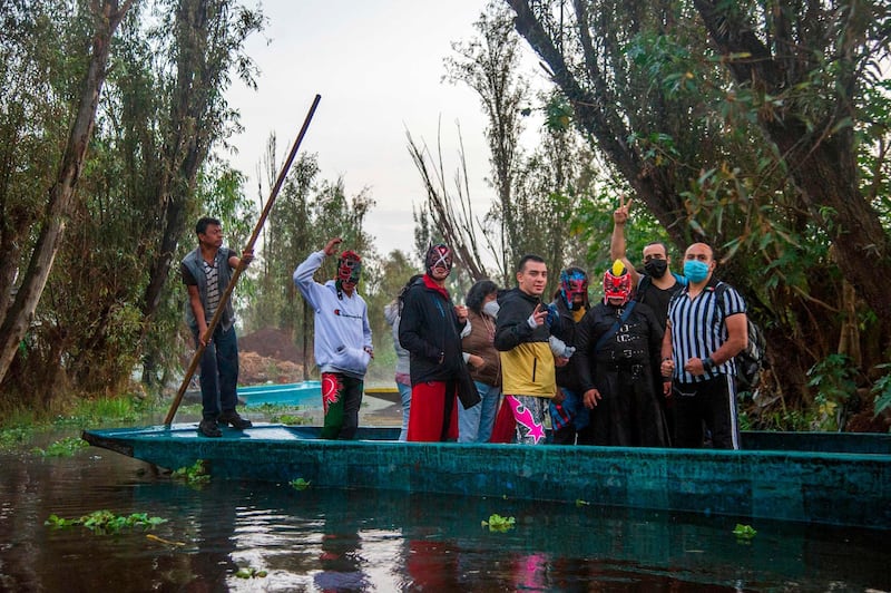 Wrestlers gesture from a typical 'trajinera' (boat), on arrival at the Chinampalucha event organized by Mexican wrestlers in the chinampas of Xochimilco in Mexico City as rings remain closed due to the Covid-19 coronavirus pandemic. AFP