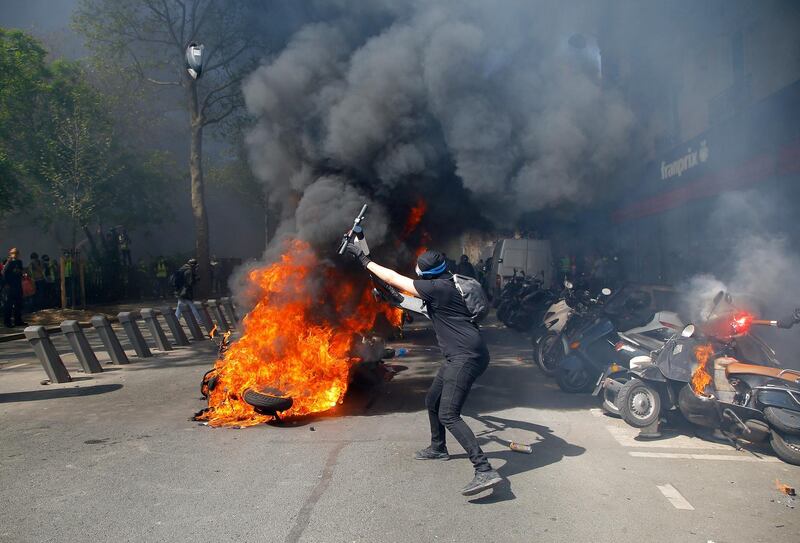 A protestor throws a scooter onto a pile of burning motorbikes during a yellow vest demonstration in Paris, Saturday, April 20, 2019. French yellow vest protesters are marching anew to remind the government that rebuilding the fire-ravaged Notre Dame Cathedral isn't the only problem the nation needs to solve. (AP Photo/Michel Euler)