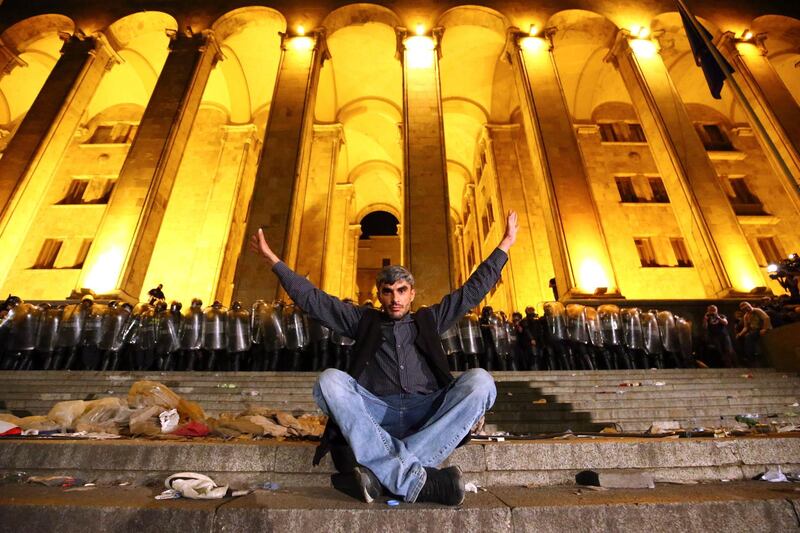 An opposition demonstrator sits in front police line at Georgian Parliament to call for the resignation of the speaker of the Georgian Parliament in Tbilisi, Georgia, Friday, June 21, 2019. Police have fired a volley of tear gas at a massive throng of protesters outside the Georgian national parliament, who are trying to storm the building and are demanding the government's resignation.(AP Photo/Zurab Tsertsvadze)