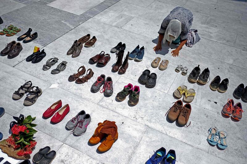 A woman prays in front of hundreds of shoes that were displayed in memory of those killed by Hurricane Maria in front of the Puerto Rican Capitol, in San Juan on June 01, 2018. Hurricane Maria, which pummeled Puerto Rico in September 2017, is likely responsible for the deaths of more than 4,600 people, some 70 times more than official estimates, US researchers said Tuesday. / AFP / Ricardo ARDUENGO

