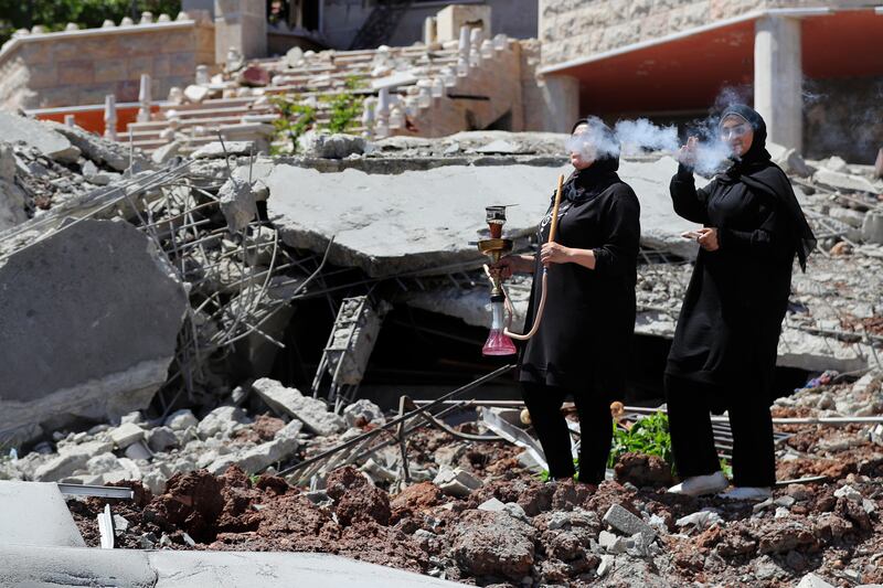 A Lebanese woman smokes a shisha as another woman flashes a victory sign, while standing on the rubble of a destroyed house that was hit by an Israeli air strike, in Aita al Shaab, a Lebanese border village with Israel, south Lebanon. AP