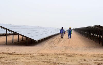 Employees walk past solar panels at the Mohammed bin Rashid Al-Maktoum Solar Park on March 20, 2017, in Dubai. - Dubai completed a solar plant big enough to power 50,000 homes as part of a plan to generate three-quarters of its energy from renewables by 2050. (Photo by STRINGER / AFP)