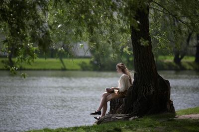 A young woman reads a book by a pond in a park near the Novodevichy Convent in Moscow during a sunny spring day on May 19, 2021. / AFP / Natalia KOLESNIKOVA
