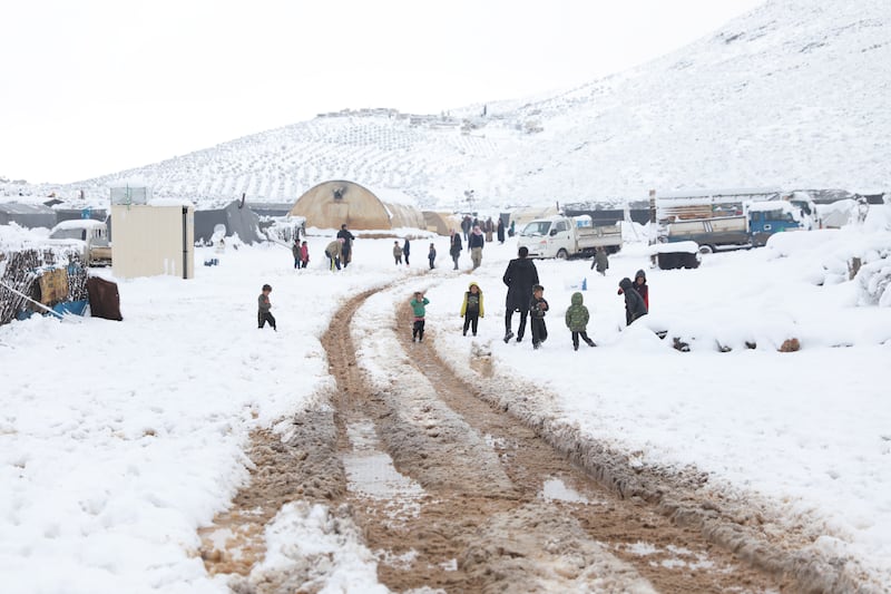 Internally displaced Syrians walk in the snow at the camp