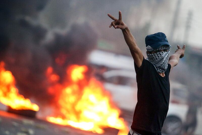 A masked Iraqi protester gestures while standing before burning tires during clashes with security forces in Basra. AFP