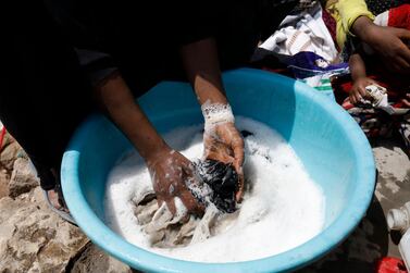 A woman washes clothes as her children sit outside a one-room home in Sanaa. EPA