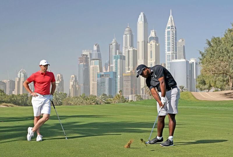 DUBAI, UNITED ARAB EMIRATES - JANUARY 23:  Rayhan Thomas of India plays his second shot on the par 5, 13th hole watched by Rory McIlroy of Northern Ireland as a preview for the Omega Dubai Desert Classic on the Majlis Course at The Emirates Golf Club on January 23, 2018 in Dubai, United Arab Emirates.  (Photo by David Cannon/Getty Images)