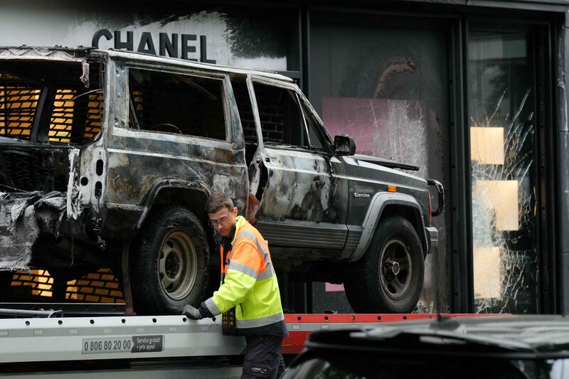 A man removes a burned-out vehicle that was used as a ram car by a team of robbers to attack a Chanel boutique near the Champs-Elysees in Paris. AFP