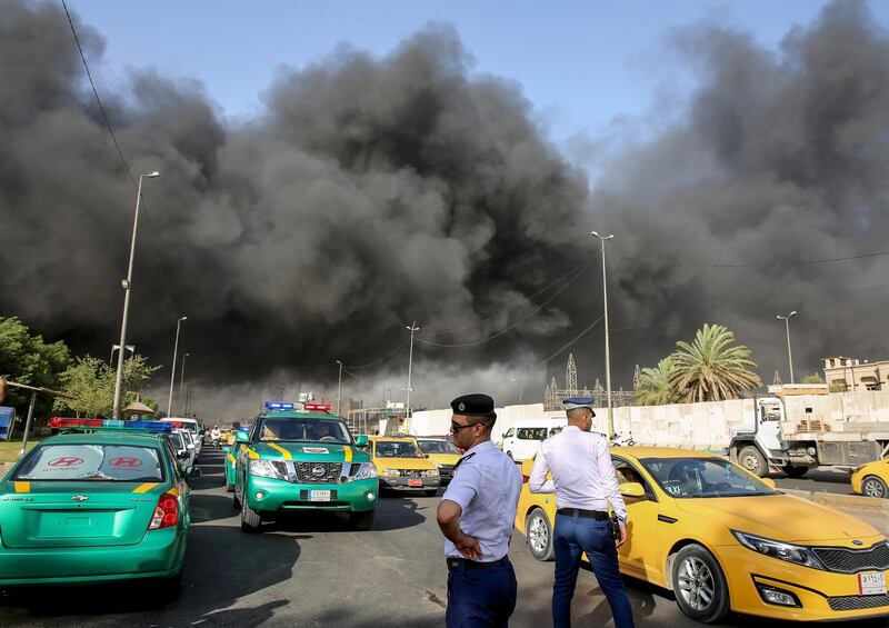 Iraqi traffic policemen stand outside the country's biggest ballot warehouse, where votes for the eastern Baghdad district were stored, as a column of black smoke billows from a the building, in the capital Baghdad on June 10, 2018. The fire ripped through the warehouse before a recount ordered by parliament was to take place, according to a security official, with the cause of the blaze not immediately known. / AFP / SABAH ARAR
