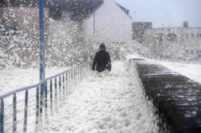A person walks as sea foam washes up on the the frontwalk in Saint-Guenole, western France, as storm Dennis sweeps accross Brittany.   AFP