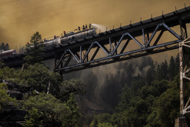 Firefighters spray water from a fire train, designed to fight wildfires, on hot spots along the tracks over Rock Creek Bridge in Plumas National Forest, California, on July 15, 2021. By David Swanson, Pulitzer Prize finalist for Feature Photography. Reuters