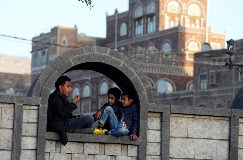 A group of Yemenis sit on a fence near historic buildings in the old quarter of Sanaa. EPA