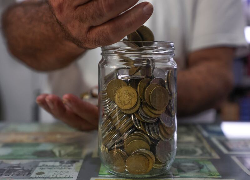 Grocery shop owner Antoine Saab puts 250 and 500 Lebanese pound coins into a jar, in Beirut.