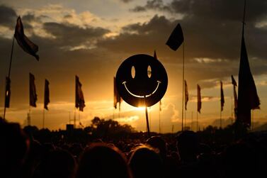 A smiley face sign is carried through the crowds as the sun sets on Glastonbury Festival. AFP
