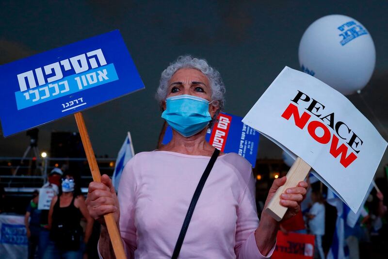 A protester, wearing a protective mask due to the COVID-19 pandemic, holds placards during a demonstration in Tel Aviv's Rabin Square to denounce Israel's plan to annex parts of the occupied West Bank.   AFP