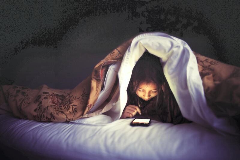 Girl using smartphone under bed covers.