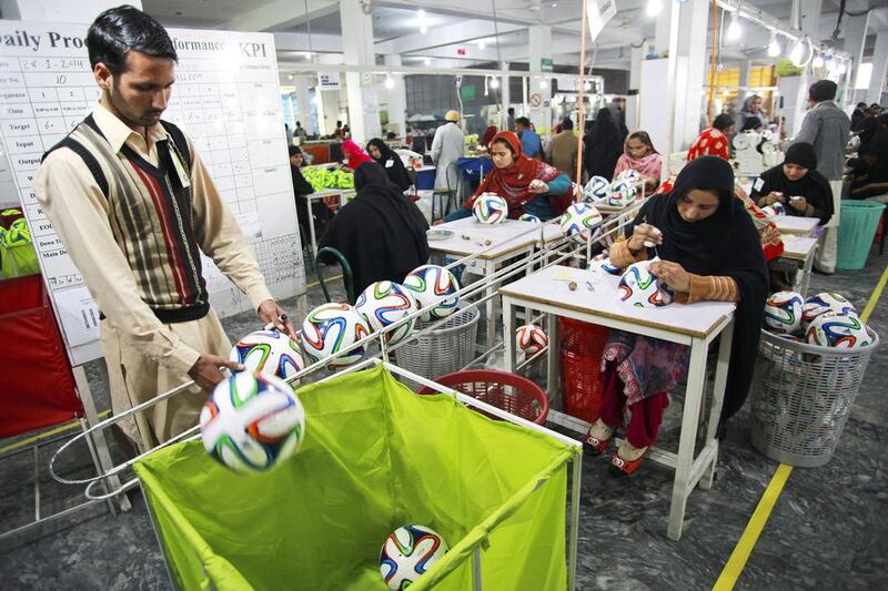 An employee places an Adidas AG "Brazuca Replica Glider" football into a trolley on the production line at the Forward Sports factory in Sialkot, Punjab. Asad Zaidi / Bloomberg

