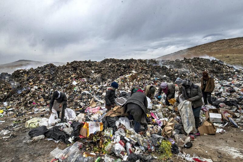 Syrians sift through a garbage dump in the countryside of Malikiya in northeast Syria, on January 17, 2021. - On the dry plains outside the city of Al-Malikiyah, a dozen people wrapped up against the cold rip open the black plastic bags, in a desperate search for something to sell, repurpose or even eat. Across the road, an oil pump swings back and forth in this resource-rich region controlled by US-backed Kurdish forces. (Photo by Delil SOULEIMAN / AFP)