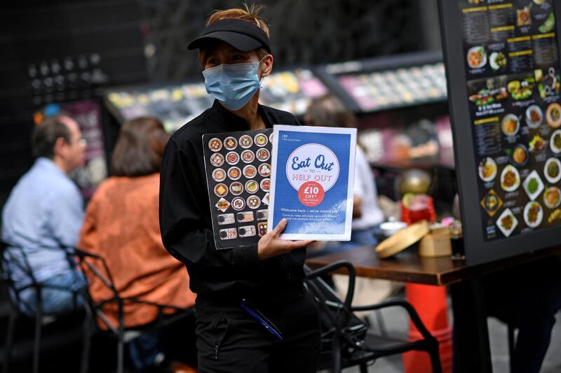 A waiter wearing a protective face mask displays "eat out to help out" information in a restaurant in the chinatown area of Soho in London on August 26, 2020, as businesses in the busy London area try to keep working despite the novel coronavirus COVID-19 pandemic. Britain's economy shrank by one fifth in the second quarter, more than any European neighbour, as the lockdown plunged the country into its deepest recession on record and tourists remain reluctant to visit because Britain is the European country worst hit by the coronavirus. 


 / AFP / Ben STANSALL

