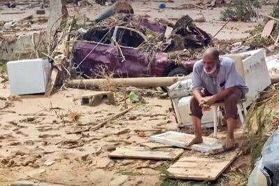 A man sits next to a destroyed vehicle in the wake of floods in Derna. Al Masar TV / AFP