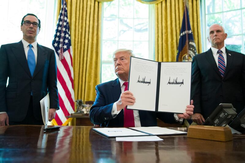 FILE - In this Monday, June 24, 2019 file photo, President Donald Trump holds up a signed executive order to increase sanctions on Iran, accompanied by Treasury Secretary Steve Mnuchin, left, and Vice President Mike Pence, in the Oval Office of the White House, in Washington. A year after President Trumpâ€™s unilateral withdrawal from the 2015 deal, the U.S. and Iran are already locked in a volatile standoff. (AP Photo/Alex Brandon, File)