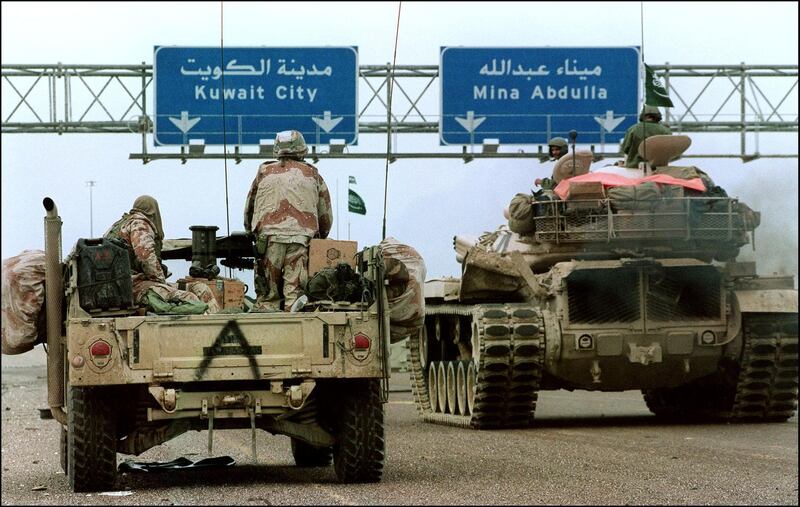 A US Hummvee jeep (l) and a Saudi tank pass under a highway sign directing them to Kuwait City 26 February 1991 during Desert Storm Allied forces offensive. (Photo by CHRISTOPHE SIMON / AFP FILES / AFP)
