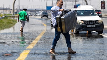 A man carries luggage through floodwater caused by heavy rain while waiting for transportation on Sheikh Zayed Road highway in Dubai, United Arab Emirates, Thursday, April 18, 2024.  The United Arab Emirates attempted to dry out Thursday from the heaviest rain the desert nation has ever recorded, a deluge that flooded out Dubai International Airport and disrupted flights through the world's busiest airfield for international travel.  (AP Photo / Christopher Pike)