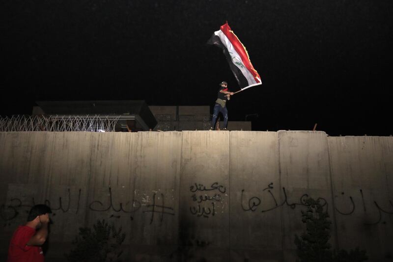 An Iraqi protester waves the Iraqi national flag as he stands on a concrete wall at the Iranian counsulate in Karbala. EPA