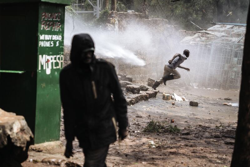 A protester takes cover from the jet of a water cannon during clashes with police forces in Kibera, Nairobi. Marco Longari / AFP Photo