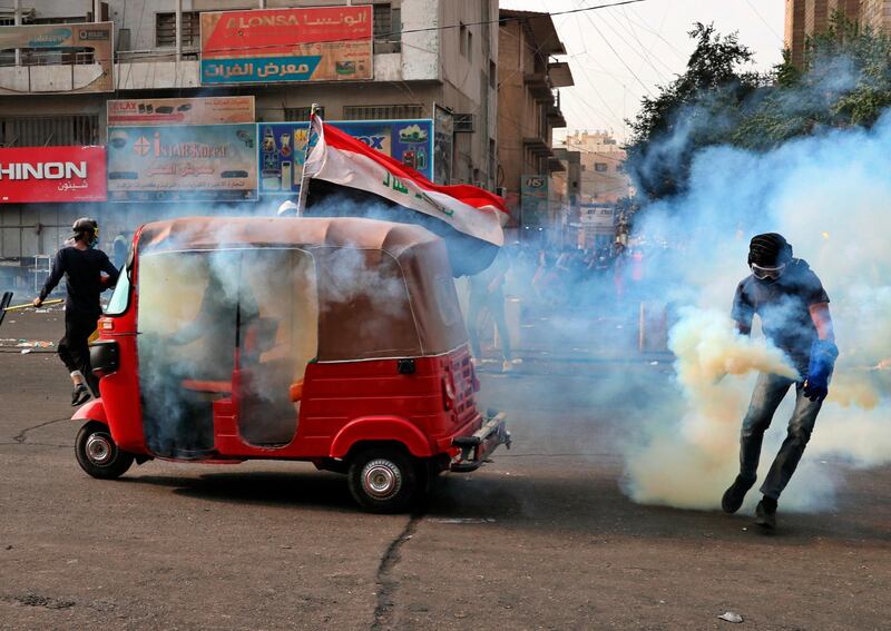 A protester carries a tear gas canister fired by riot police during clashes in Baghdad, Iraq. AP Photo