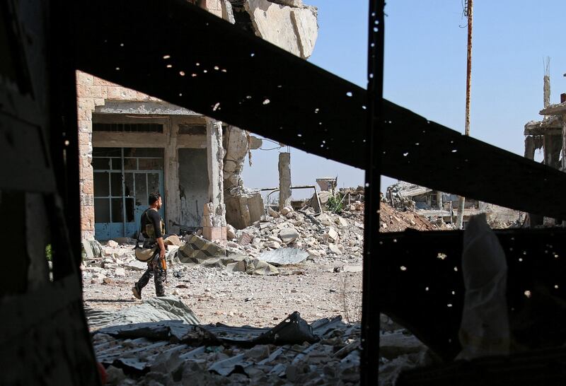 A Free Syrian Army fighter carries his weapon as he walks past damaged buildings in a rebel-held part of Deraa city in Syria's south-west on July 9, 2017. Alaa Al Faqir / Reuters