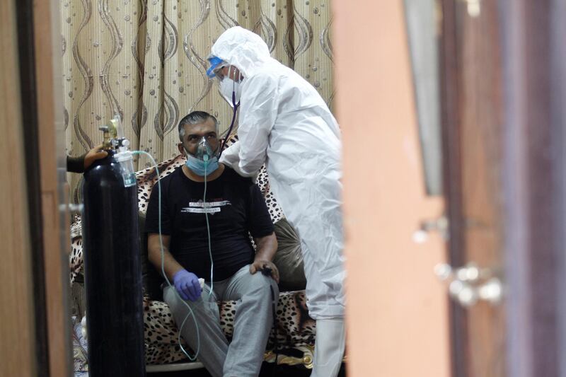 An Iraqi volunteer in a protective suit takes care of a patient infected with coronavirus, as he provides him with oxygen at home in Najaf. Reuters
