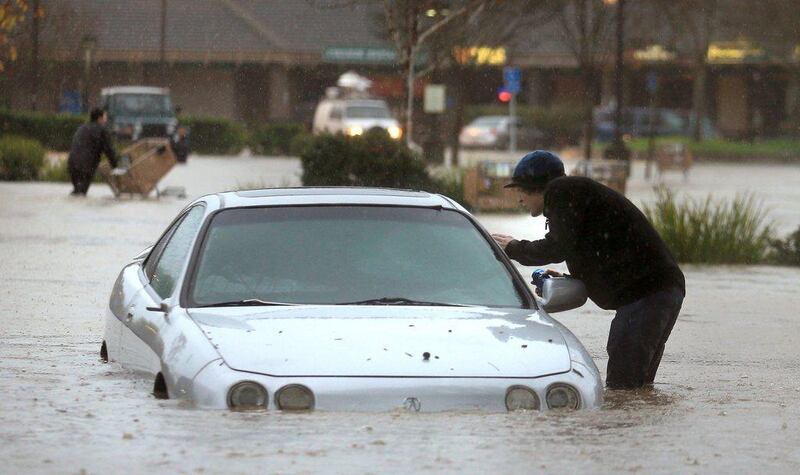 A resident checks for people in a vehicle submerged in floodwaters on Vine Street in Healdsburg California. Kent Porter / Santa Rosa Press Democrat / Associated Press