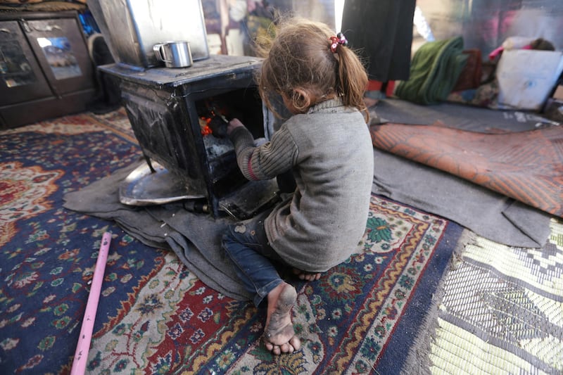 An internally displaced girl, who fled from western Aleppo countryside, sits next to a heater inside a tent in Afrin, Syria. REUTERS