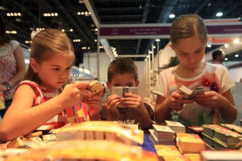 ABU DHABI - 02APRIL2012 - Kids  Amaya, right, Troy, centre, and Jaci Garrick looks at the World's tiniest books at a stall in the Abu Dhabi International Book Fair yesterday at Abu Dhabi National Exhibition Centre. Ravindranath K / The National 
