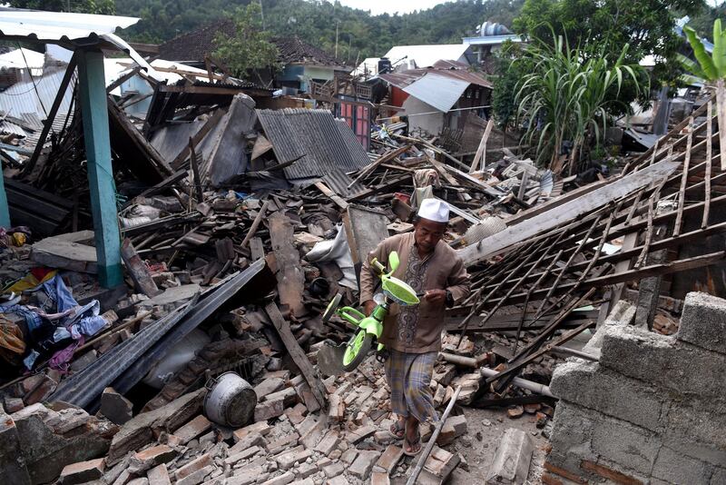 A man carries a small bicycle through the ruins of houses damaged by an earthquake in West Lombok, Indonesia,  August 6, 2018 in this photo taken by Antara Foto.  Antara Foto/Zabur Karuru / via REUTERS  ATTENTION EDITORS - THIS IMAGE WAS PROVIDED BY A THIRD PARTY. MANDATORY CREDIT. INDONESIA OUT.