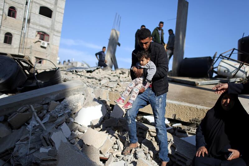 A Palestinian man carries a child as he walks through the debris of a house destroyed by an Israeli air strike, in the southern Gaza Strip. Reuters