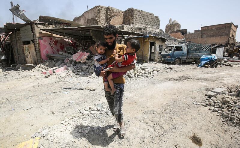 TOPSHOT - A man carries two children in his arms hile fleeing from the Old City of Mosul on July 2, 2017, as Iraqi government forces continue their offensive to retake the city from Islamic State (IS) group fighters. / AFP PHOTO / AHMAD AL-RUBAYE