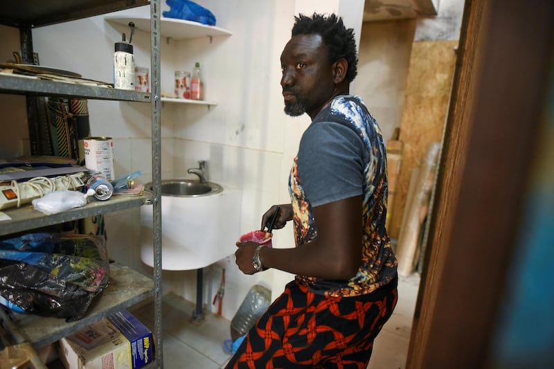 Senegalese artist Omar Ba mixes paint in a plastic cup in a storage area of his studio. Cooper Inveen / Reuters