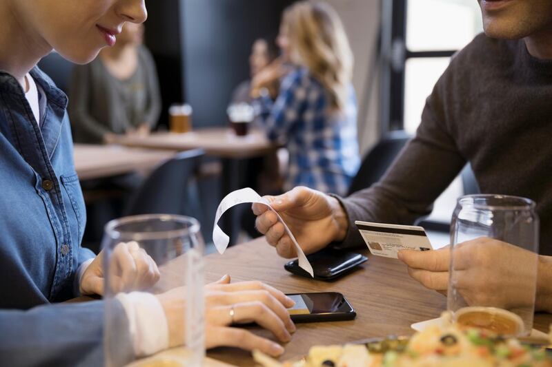 Close up couple with credit card paying bill calculating tip with smart phone in brewery restaurant. Getty Images