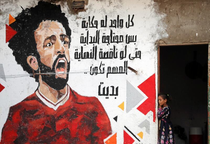 An Egyptian girl looks out from her house beside a mural depicting Liverpool player Mohamed Salah with a message that reads 'Everyone has a story but needs a start. Be ready and start your dream' at a slum area in Cairo, Egypt'. Reuters