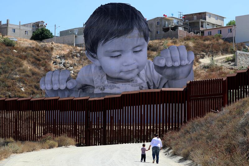 A small boy walks with his mother in front of French artist JR's image of an inquisitive baby looking into the United States over the US - Mexico border wall, near Tecate, California. Mike Blake / Reuters.